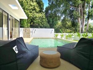Espace detente exterieur avec poufs au bord de la piscine et environnement tropical a koh samui