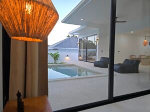 Vue depuis l'interieur vers la terrasse couverte avec poufs d'exterieur et la piscine privee d'une villa a koh Samui