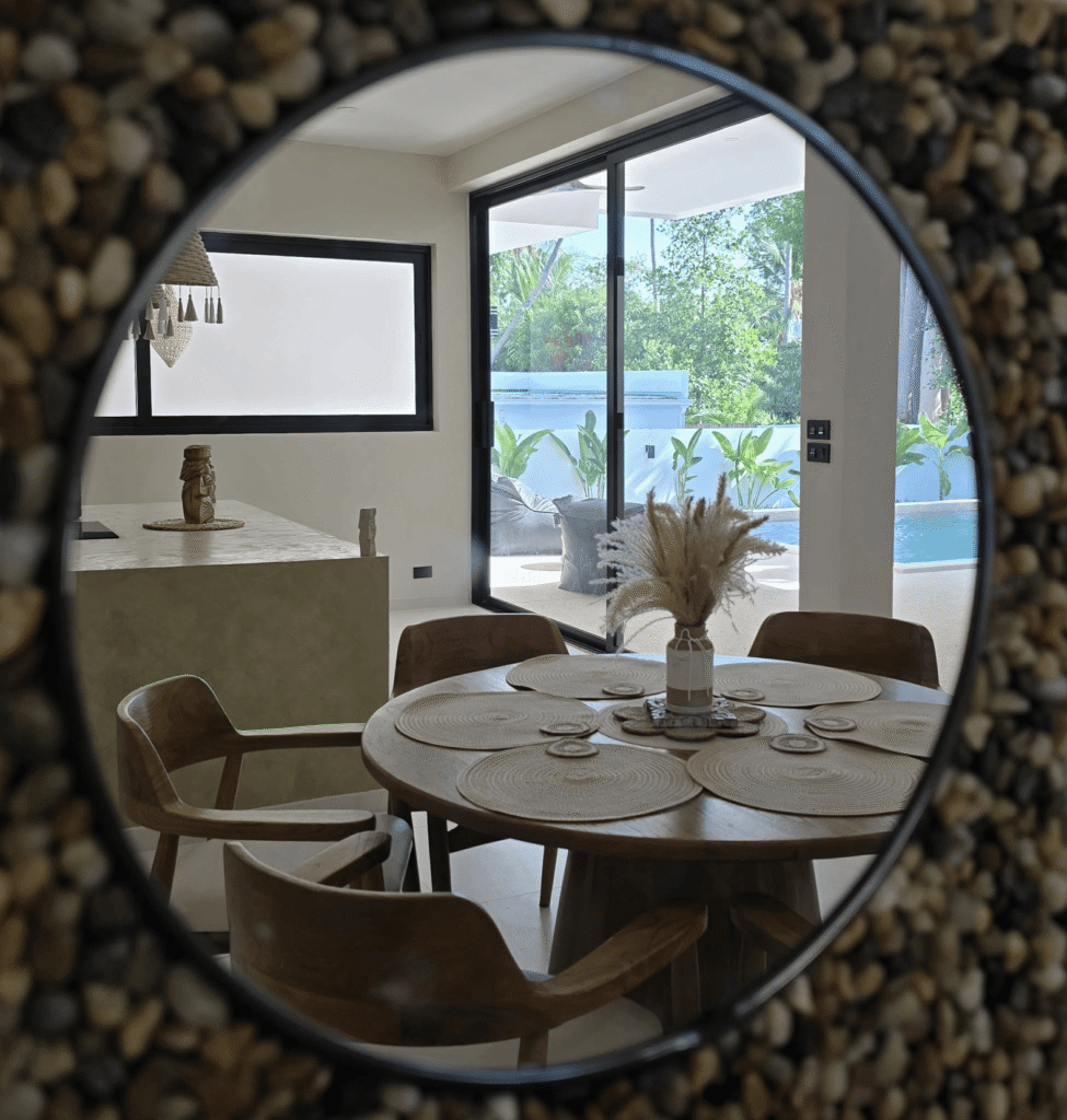 Reflet dans un miroir rond montrant un coin repas de villa ouverte et un espace de vie donnant sur une piscine